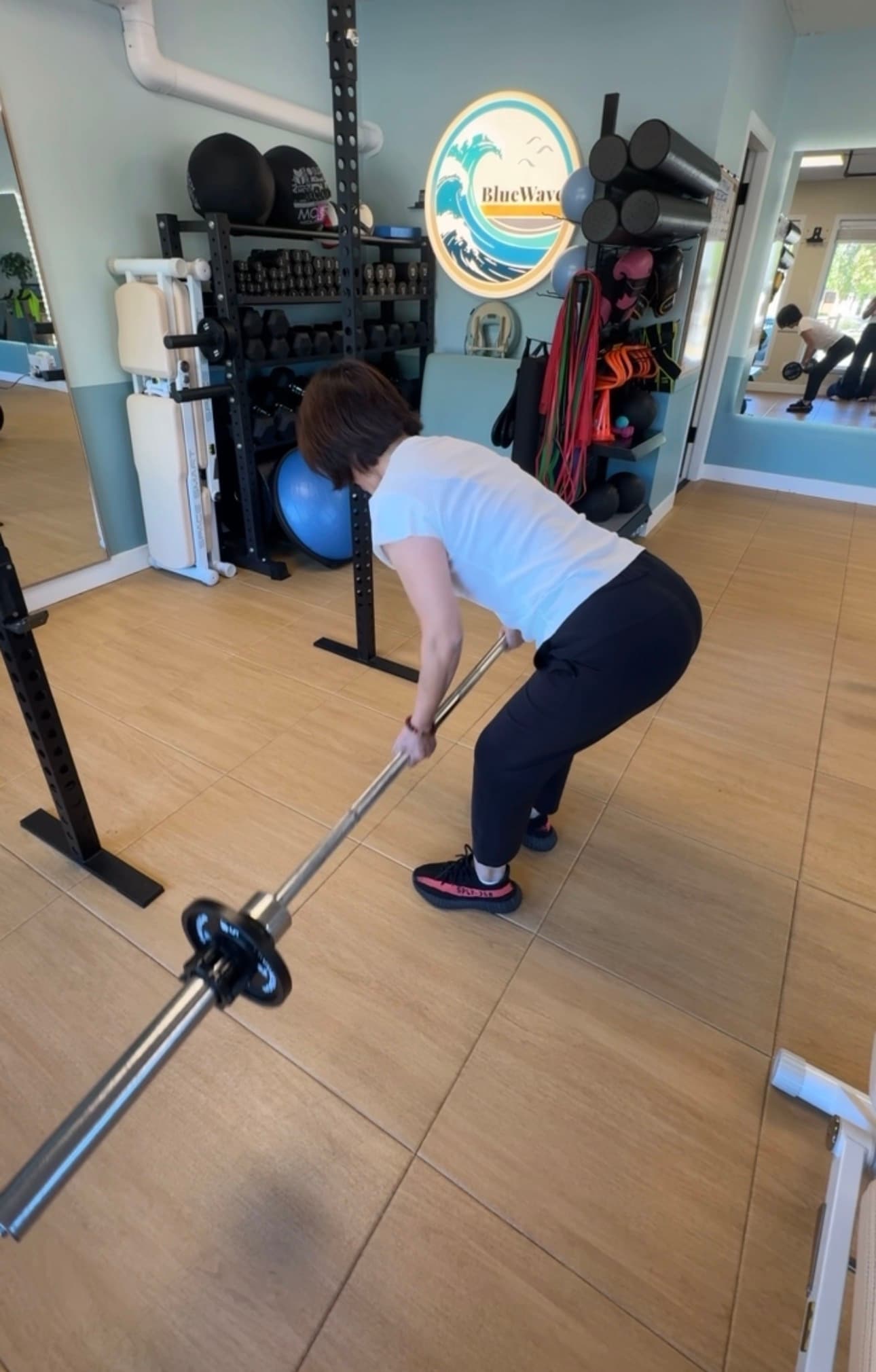 Woman in a white shirt performs a landmine row exercise in a well-equipped gym.