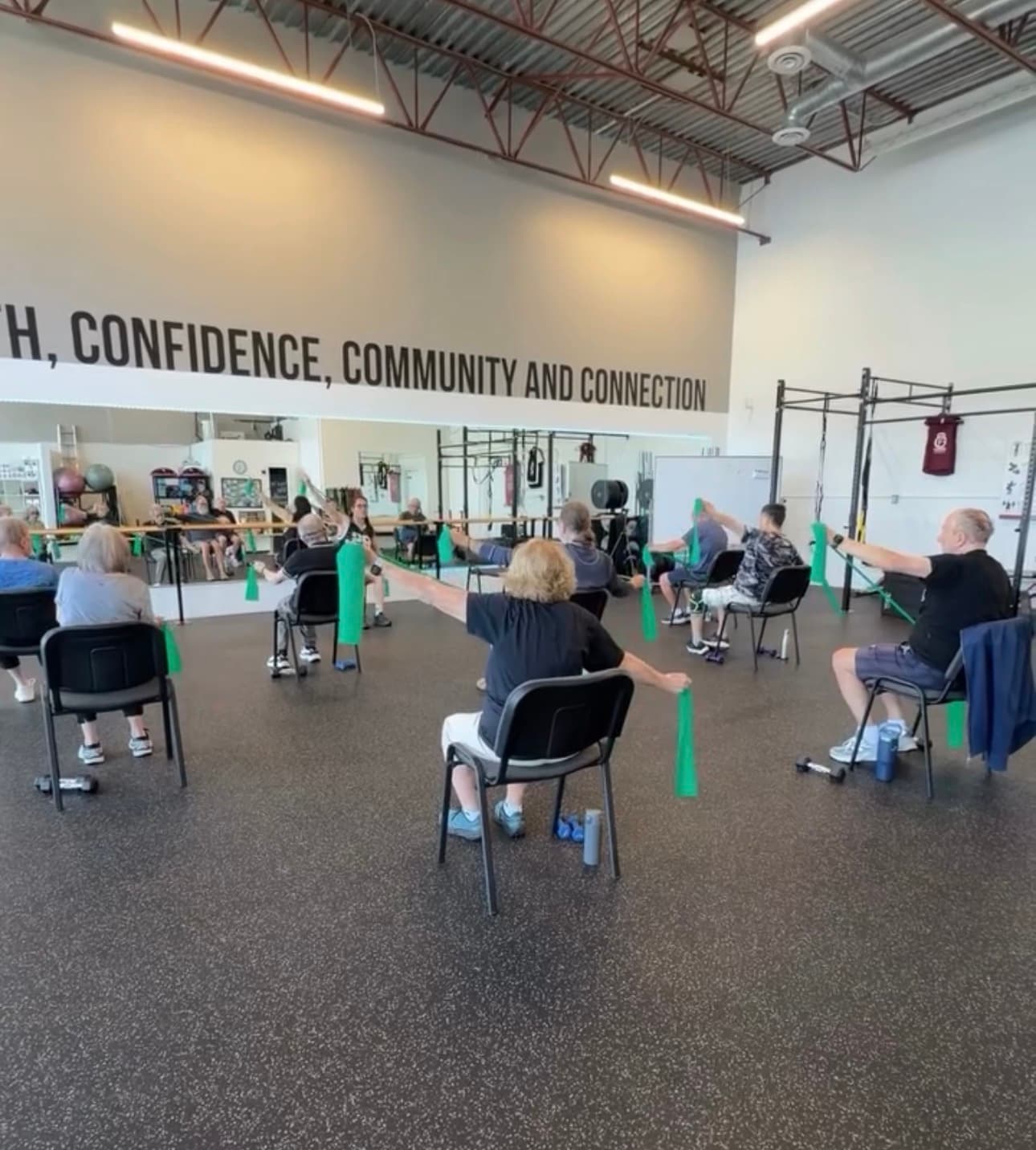 Seniors performing seated exercises with green resistance bands in a gym under motivational wall text.