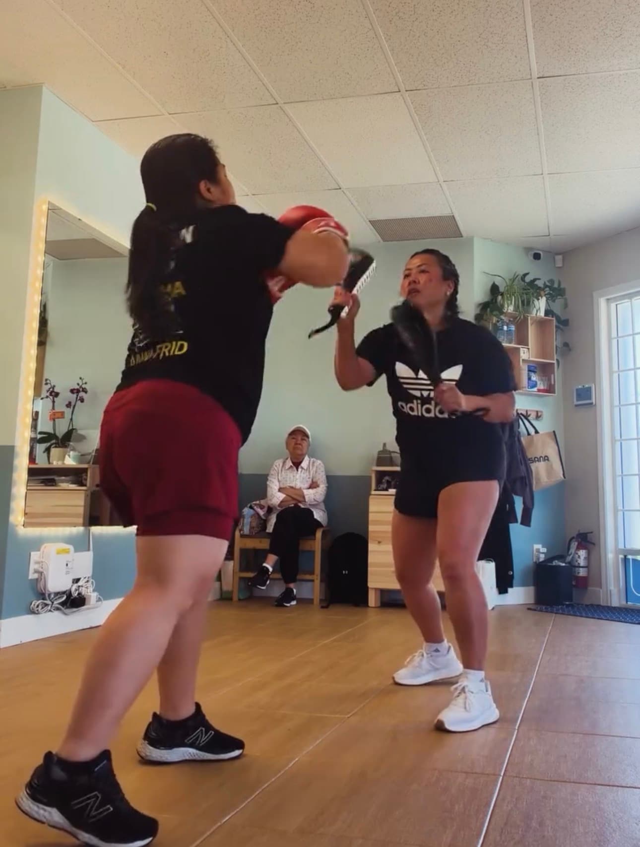Two women practice boxing in a studio, one punching focus pads held by the other.