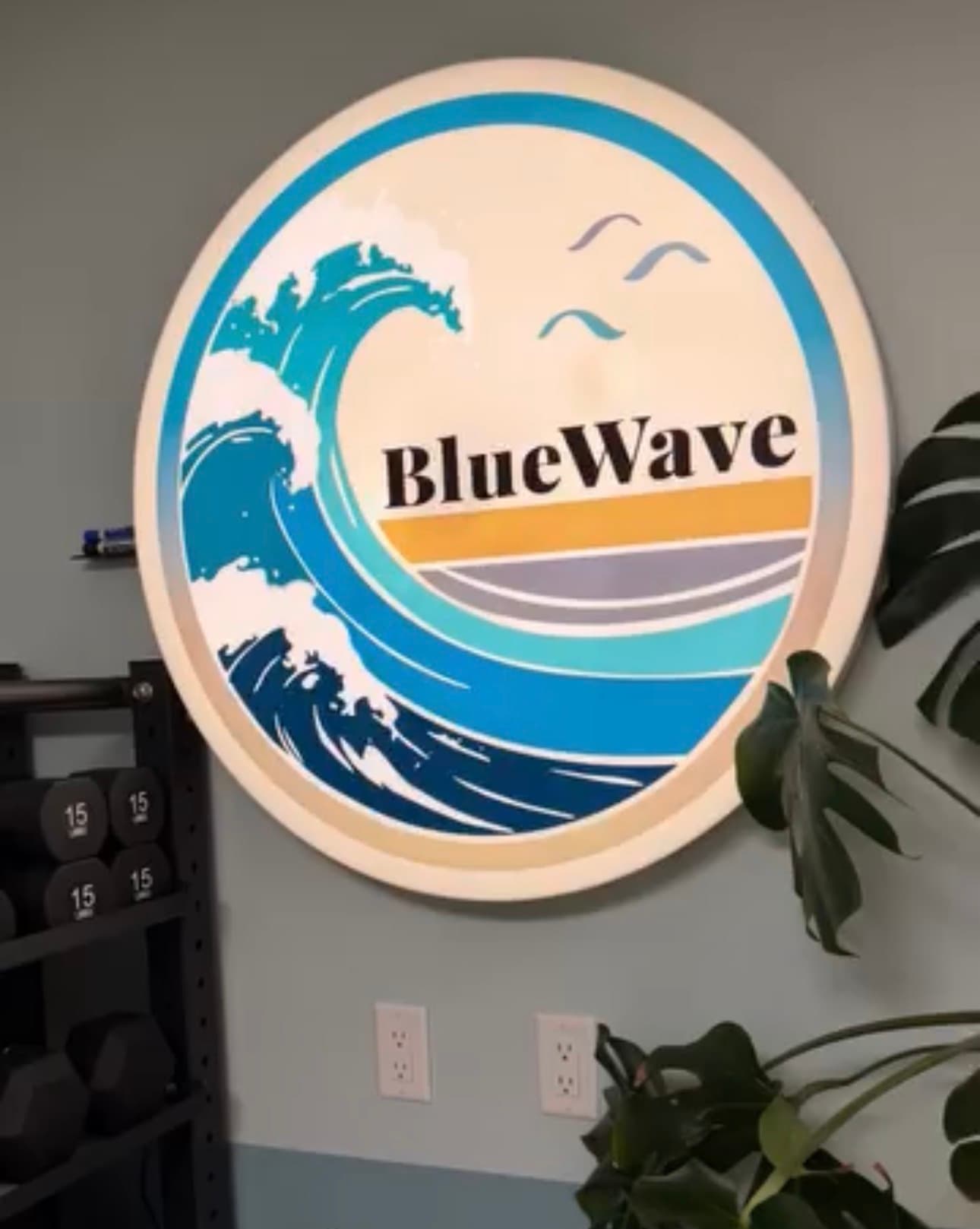 Circular BlueWave sign featuring a stylized ocean wave and text, mounted on a gym wall.