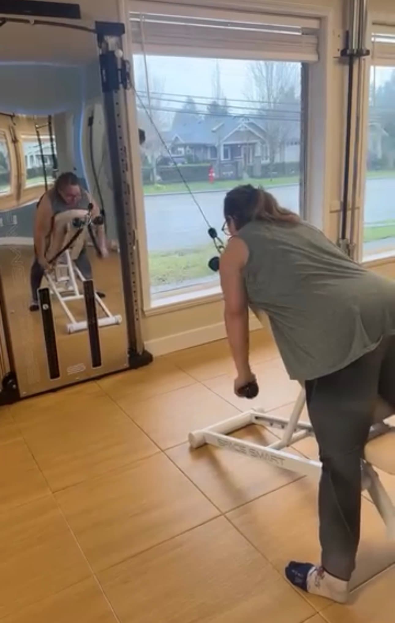 Woman performs cable rows on a weight bench in a home gym with mirrors.