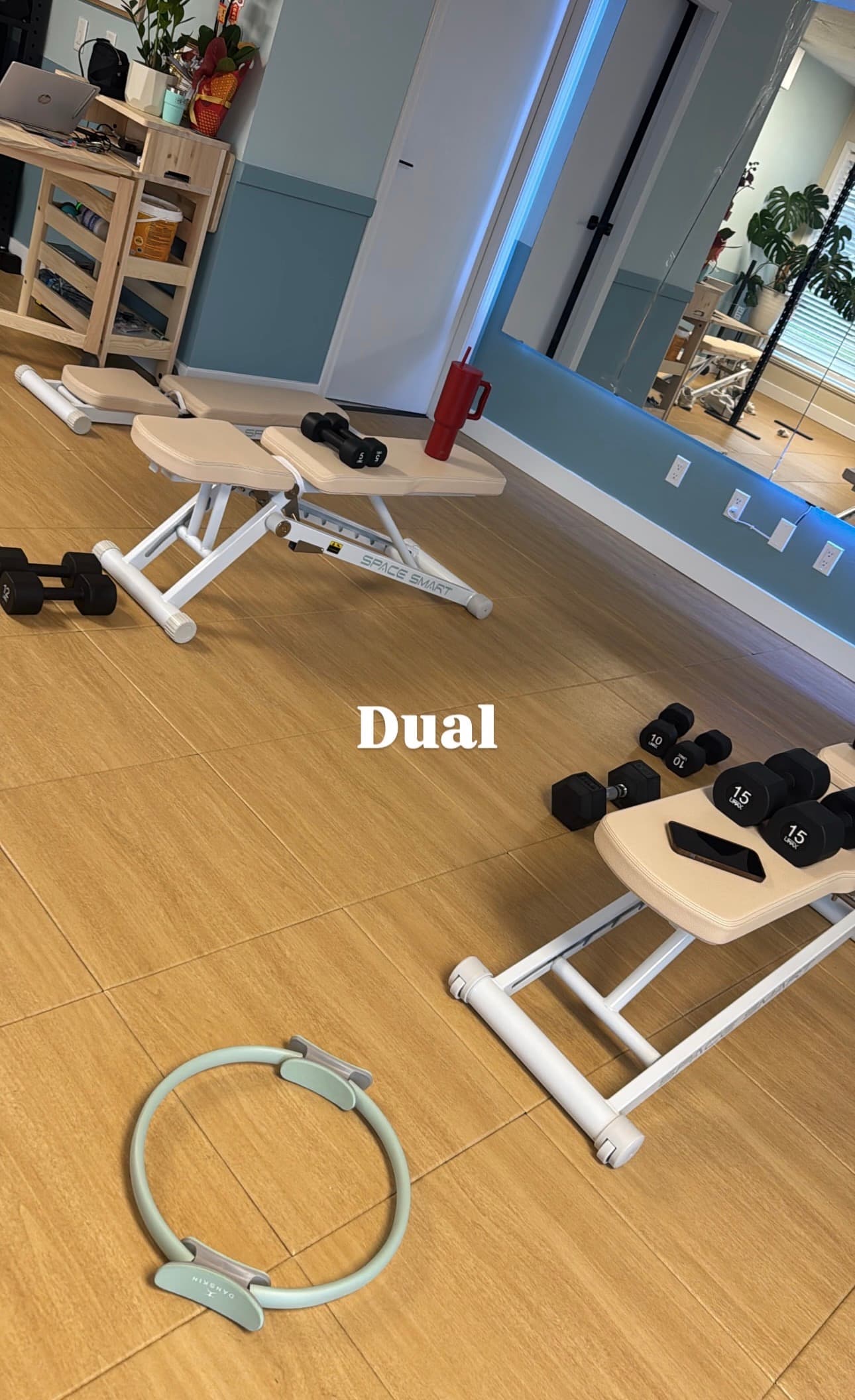 Two white workout benches, various dumbbells, and a Pilates ring on light wood flooring.