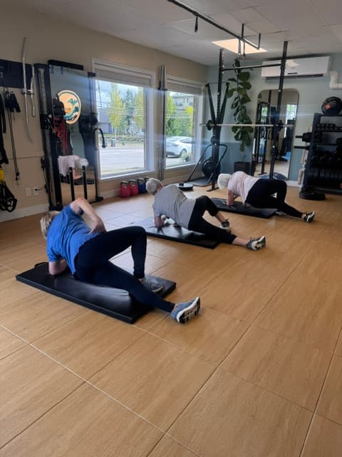 Three women performing side plank exercises on black mats in a bright, modern fitness gym.