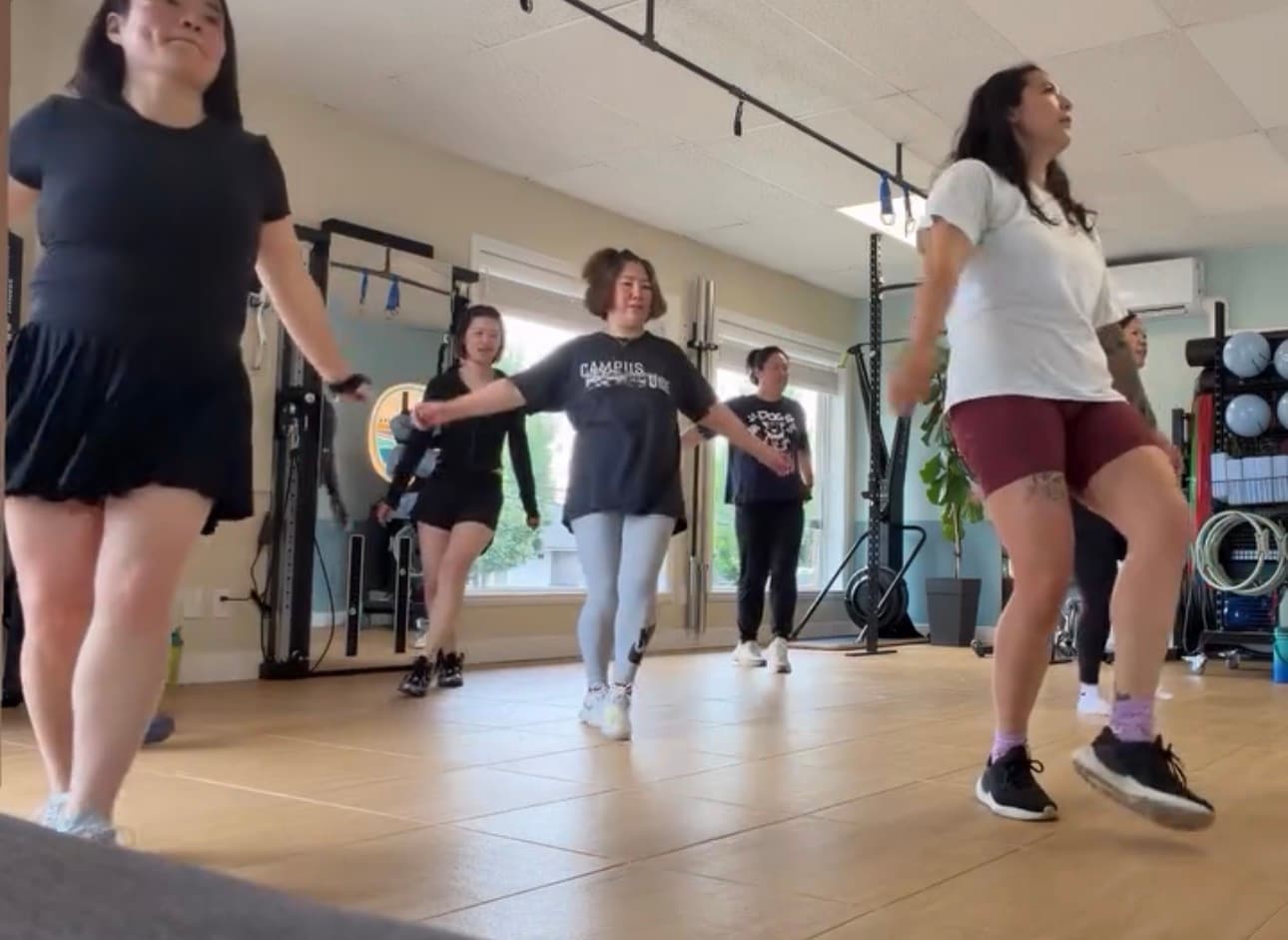 Women in athletic clothing perform a synchronized dance routine in a bright fitness studio.