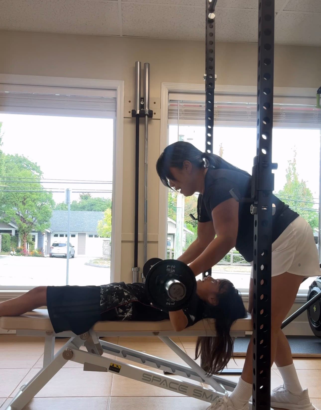 Woman spotting a young girl performing a barbell bench press on a weight bench.